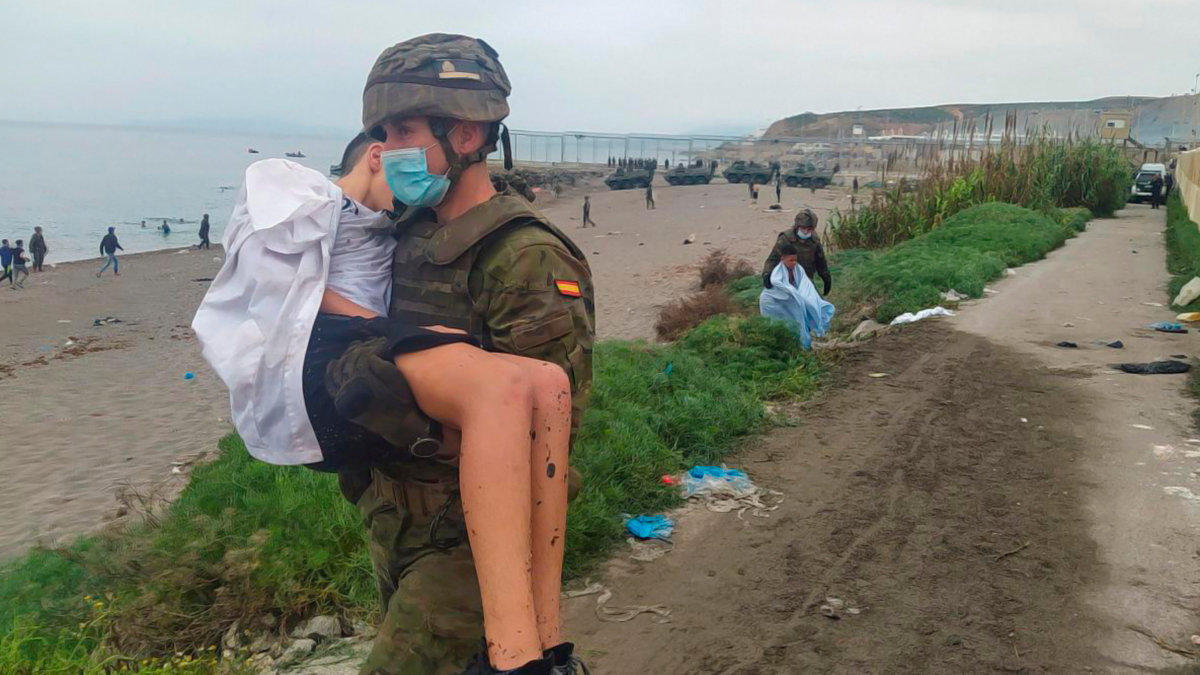 Un miembro del Ejército español ayuda a un menor inmigrante en una de las zonas fronterizas de Ceuta. Foto: Reduan / EFE