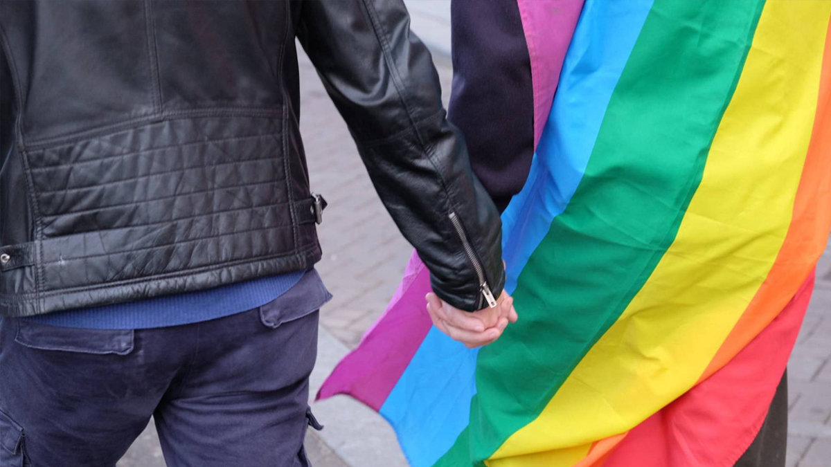 Imagen de archivo donde una pareja se coge la mano con la bandera multicolor. PeriódicoCLM