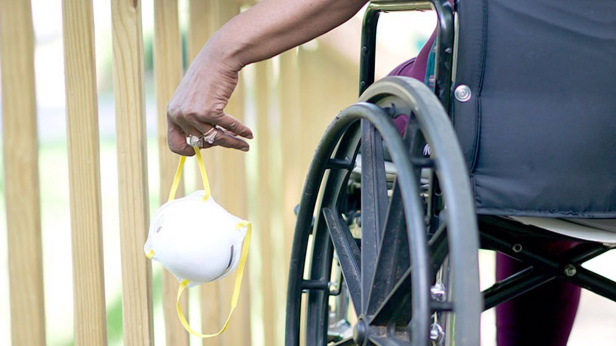 Imagen de una mujer mayor en silla de ruedas sujetando una mascarilla. — ARCHIVO