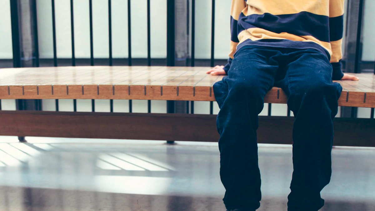 Imagen de archivo de un niño sentando solo en un banco. — UNSPLASH